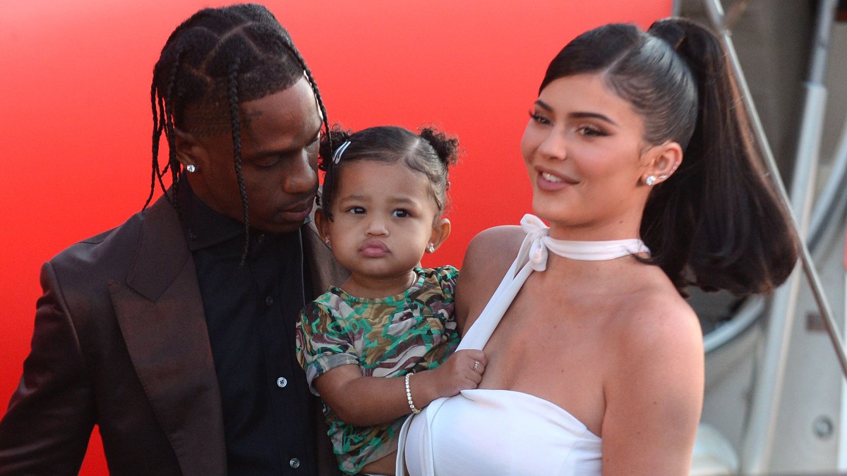 Travis Scott standing next to Kylie Jenner and their daughter Stormi Webster in front of a plane