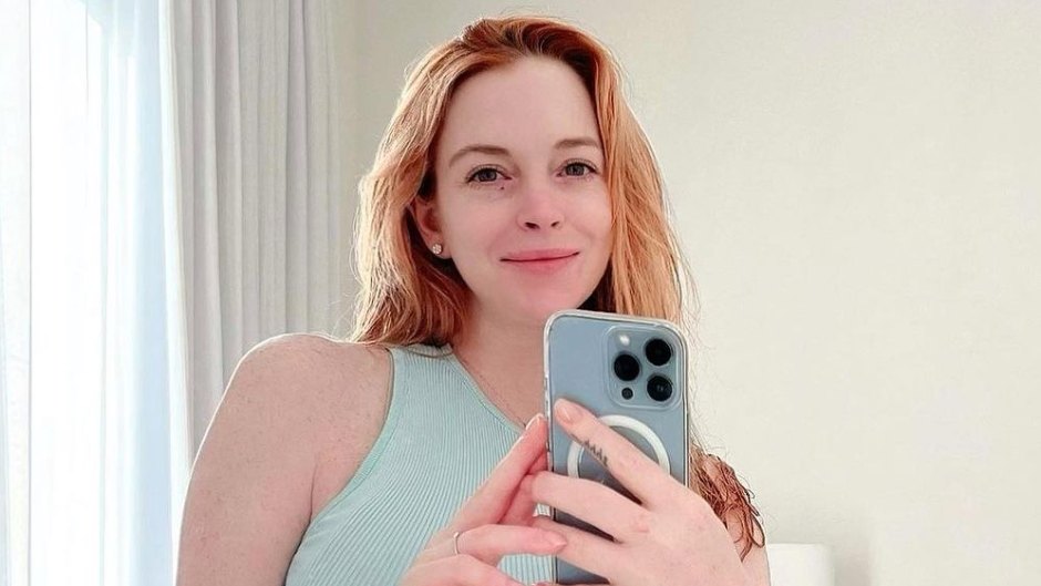 Lindsay Lohan snapping a selfie in a green crop top shirt and gray shorts