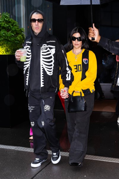 Kourtney Kardashian holds hands with Travis Barker while wearing a yellow sweatshirt.