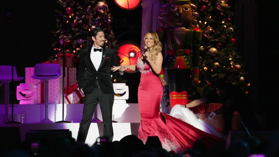 Mariah Carey wears a red dress onstage next to Bryan Tanaka who's wearing a tuxedo.