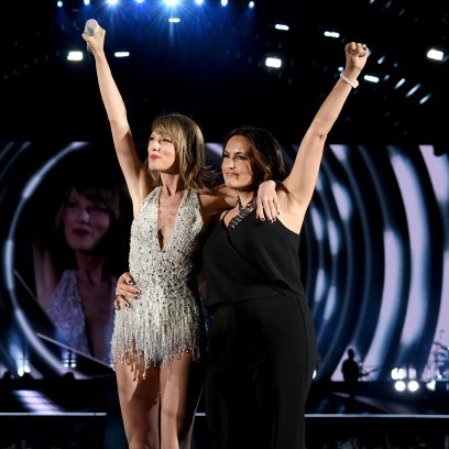 Taylor Swift and Mariska Hargitay stand on stage with their arms raised.