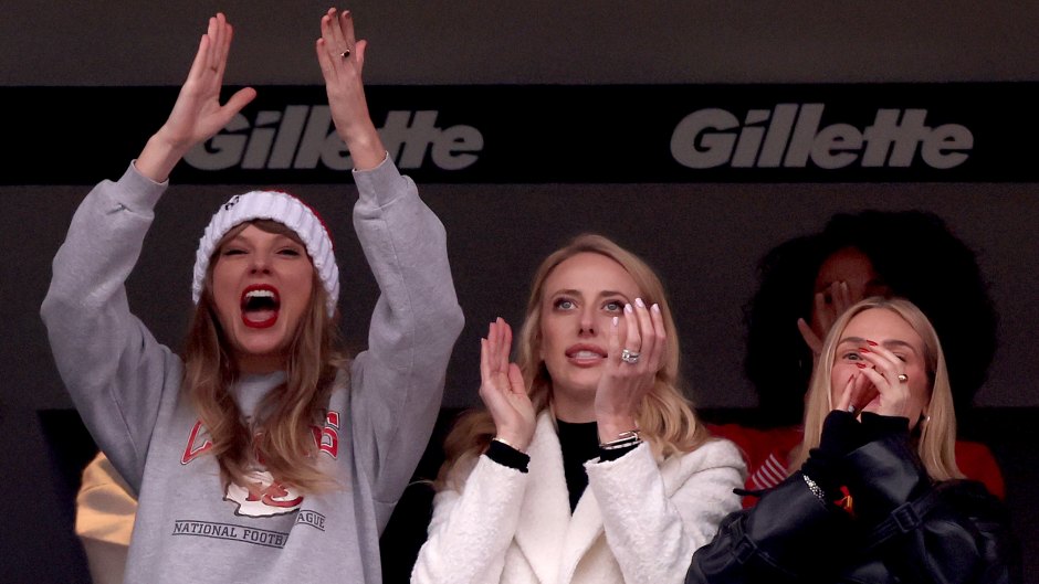Taylor Swift cheers on Travis Kelce in the suites at Gillette Stadium wearing a Chiefs sweatshirt and red and white beanie.