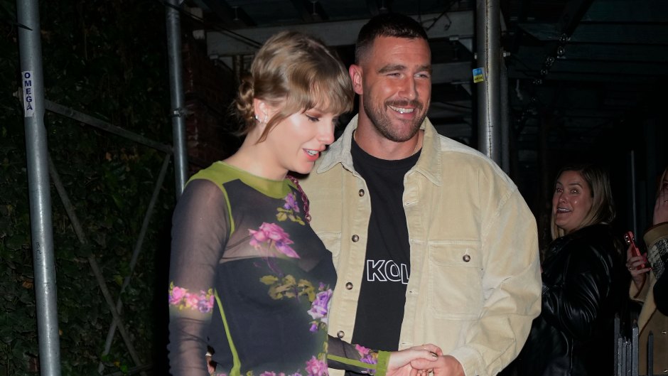 Travis Kelce wearing a tan jacket holding hands with Taylor Swift