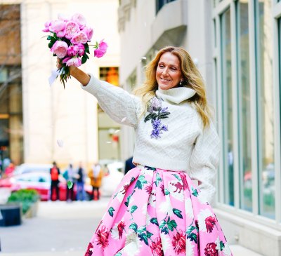 Celine Dion holds a bouquet of flowers while wearing a sweater and pink floral dress