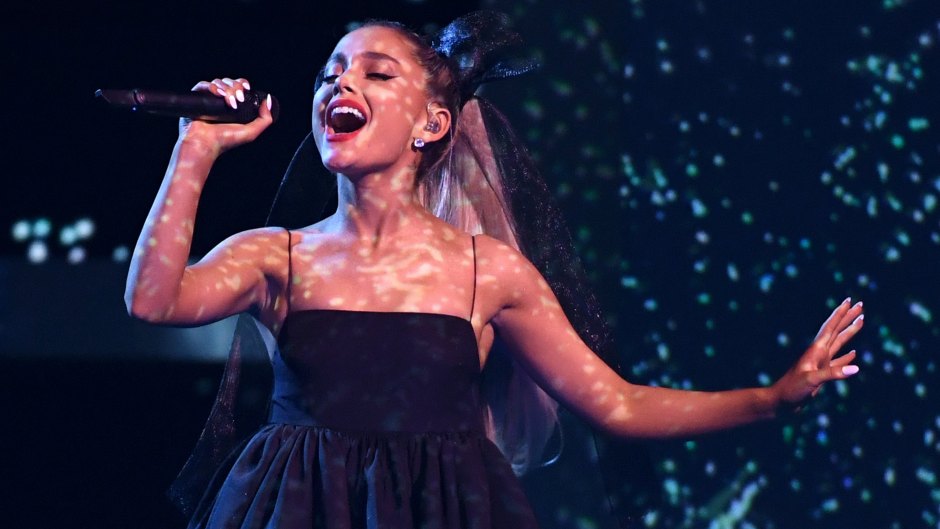 Ariana Grande holds a mic while singing in a black dress