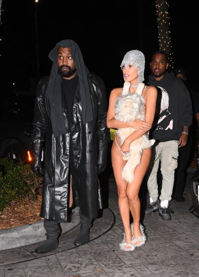 Bianca Censori wears a stuffed cat affixed to her torso next to Kanye West in an all black outfit.