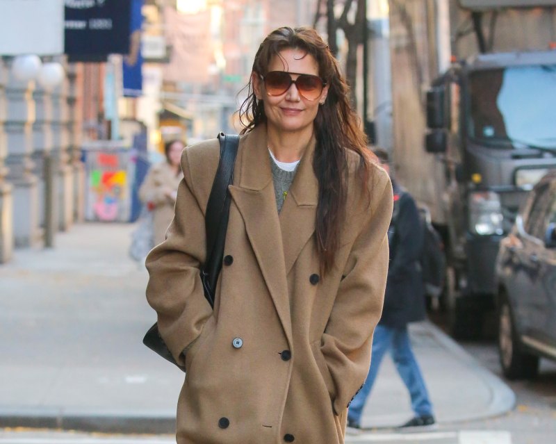 Katie Holmes walking in New York City while wearing a camel colored coat and sunglasses.