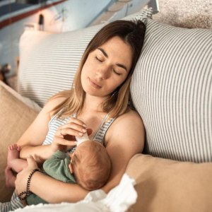 New mom nursing a newborn and enjoying a gift basket filled with food and practical gifts
